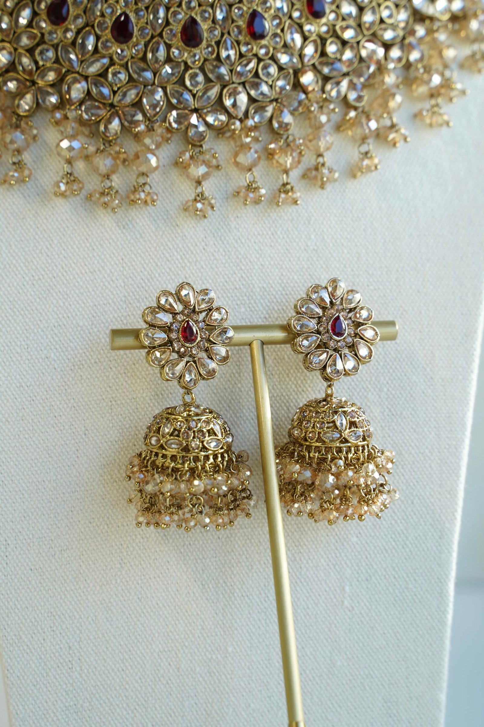 Seyora two-layer South Asian bridal necklace set featuring maroon stone and crystal bead settings with a choker, longer necklace, matching jhumka earrings, and a maang tikka