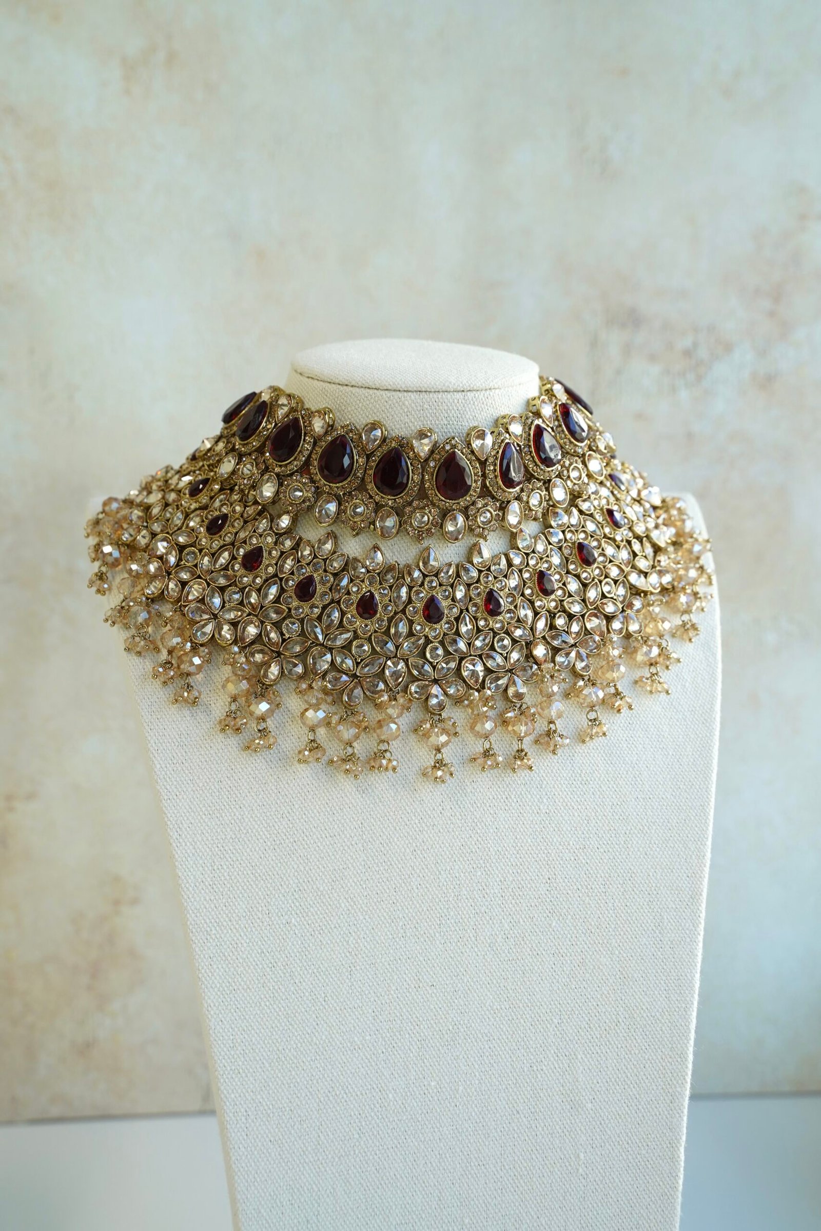 Seyora two-layer South Asian bridal necklace set featuring maroon stone and crystal bead settings with a choker, longer necklace, matching jhumka earrings, and a maang tikka