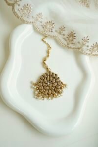Detailed close-up of a circular antique gold maang tikka with a central crystal stone and hanging delicate white pearl clusters.