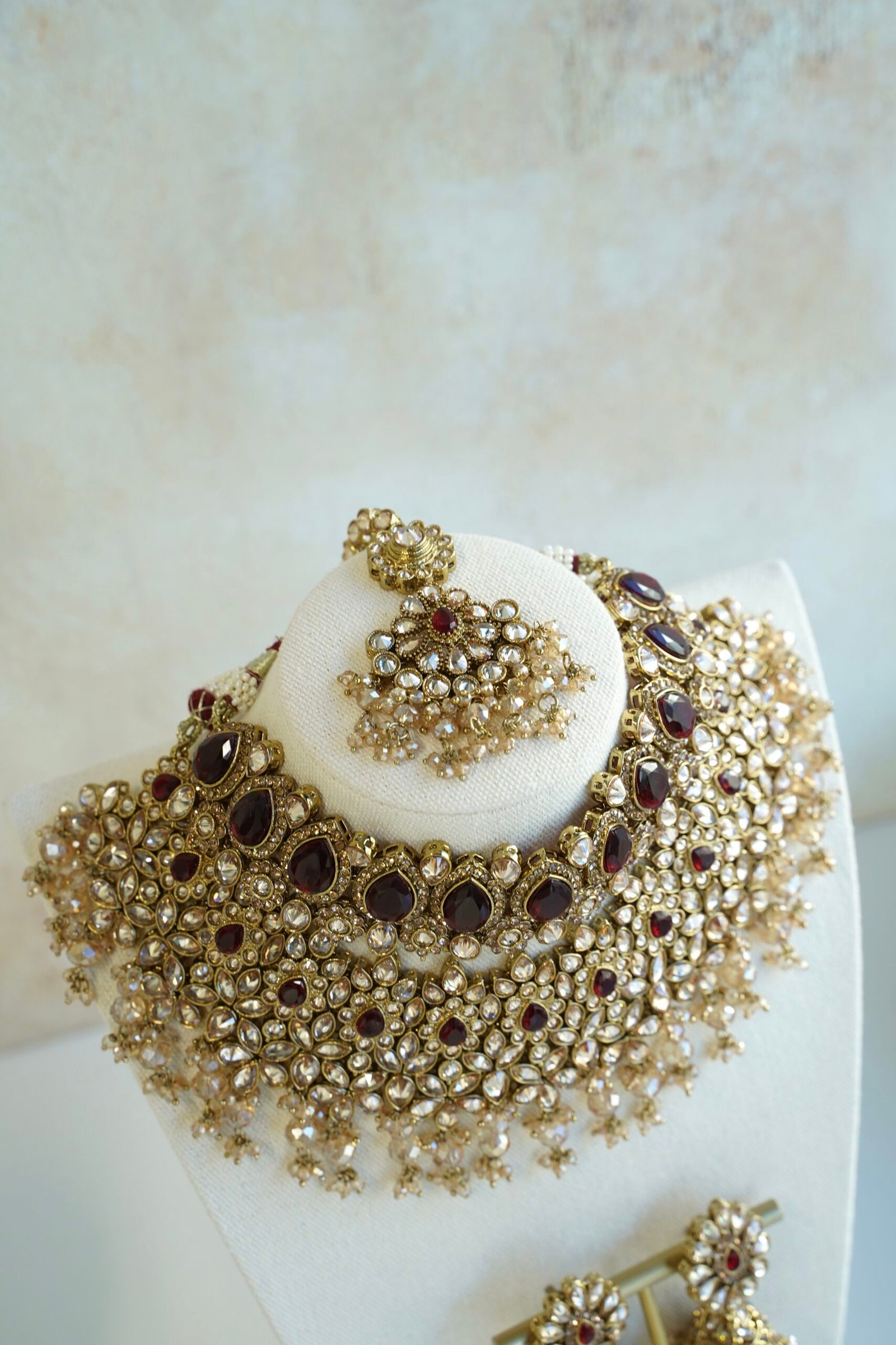 Seyora two-layer South Asian bridal necklace set featuring maroon stone and crystal bead settings with a choker, longer necklace, matching jhumka earrings, and a maang tikka