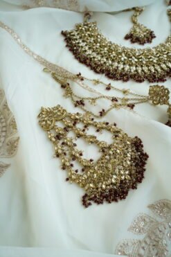 Seyora Jewels bridal jewelry set featuring a champagne stone necklace with maroon beads, matching jhumka earrings with kanchain, maang tikka, and passa.
