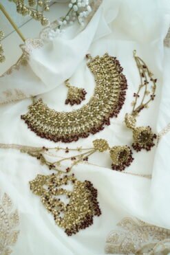 Seyora Jewels bridal jewelry set featuring a champagne stone necklace with maroon beads, matching jhumka earrings with kanchain, maang tikka, and passa.
